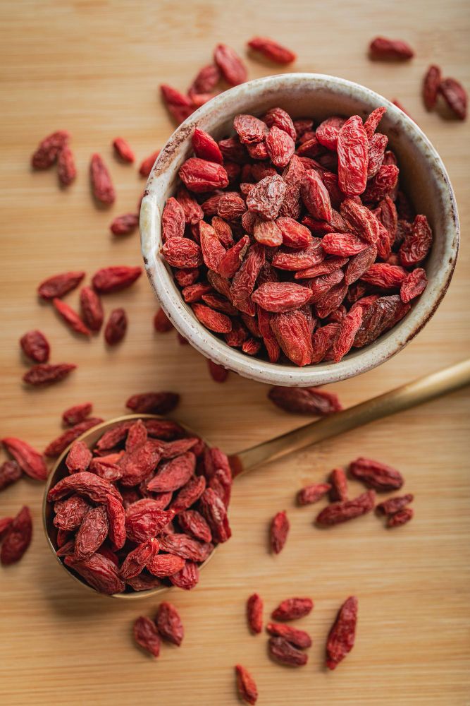 Fructe de goji uscate în două boluri, pe o masă de lemn